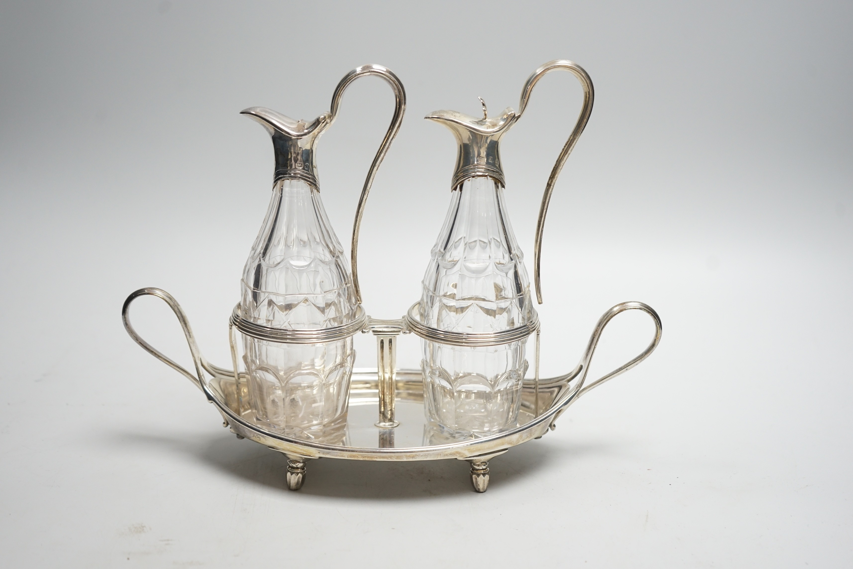 A George III silver navette shaped two handled oil and vinegar stand, with two matching silver mounted cut glass bottles (one thumbpiece missing), John Scofield, London, 1787, length 28cm, stand, 13.7oz.